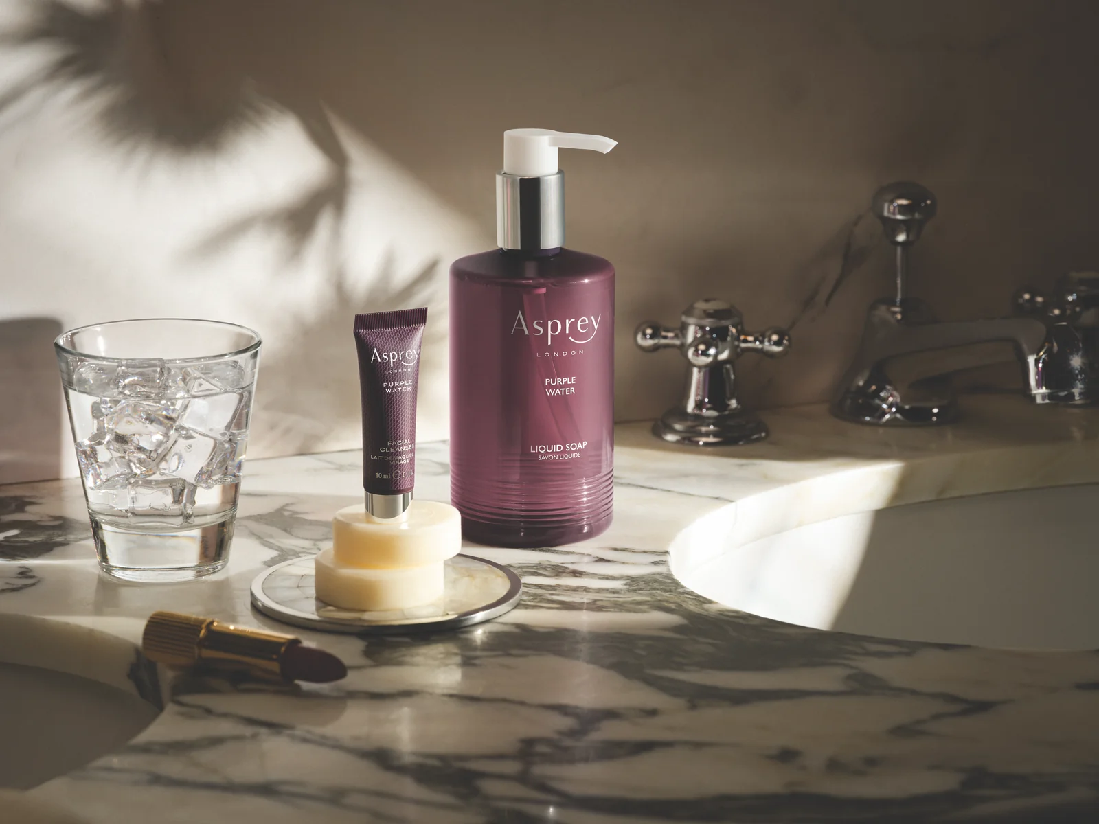 Cosmetice Asprey Purple Water pe un lavoar de marmură, într-o baie de hotel